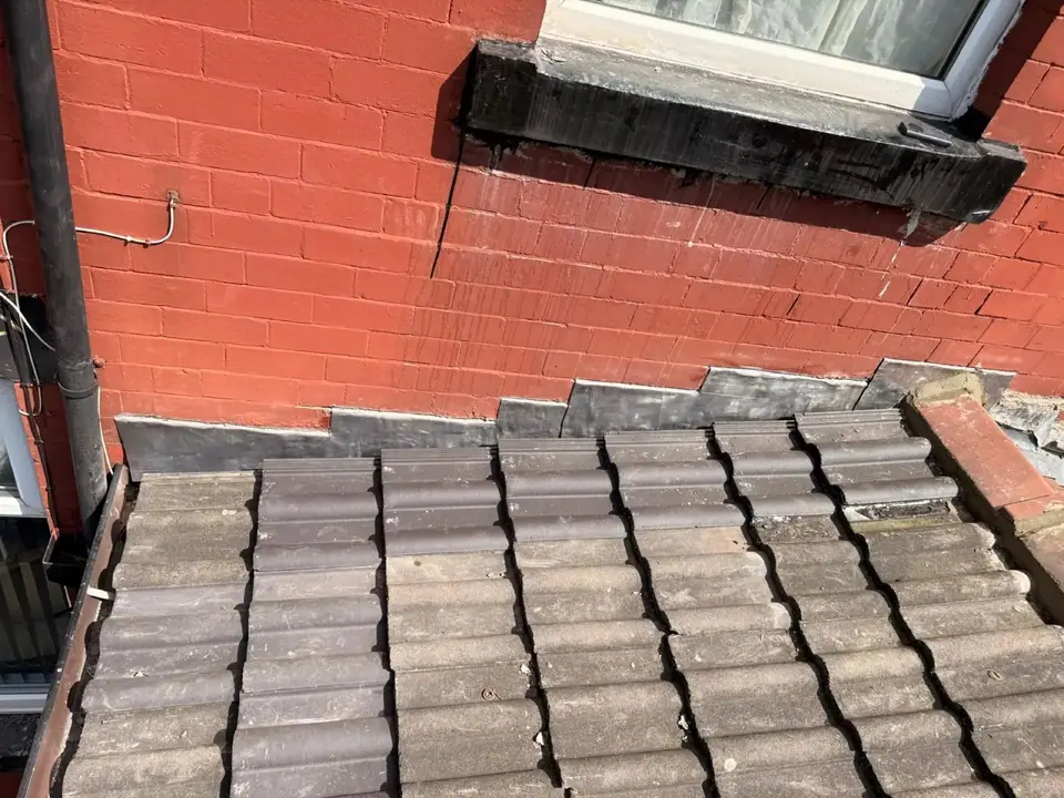 Lead flashing dressed along a tiled roof and red brick wall